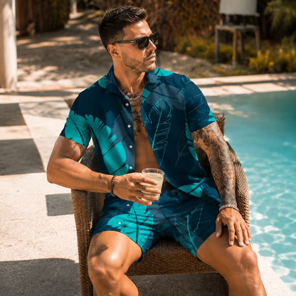 A man wearing a matching teal and dark blue tropical leaf print short-sleeve button-up shirt and shorts sits in a wicker chair by a swimming pool, holding a drink.