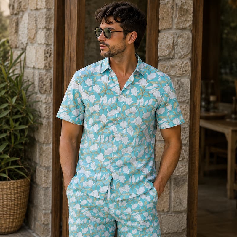 A man wearing a matching two-piece lounge set with a light blue and white tropical floral print, standing in front of a rustic stone wall doorway.
